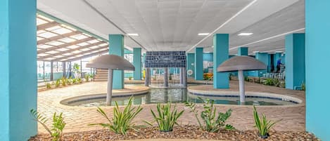Zona de piscina con una fuente central, suelo de baldosas y bordes con azulejos azules.