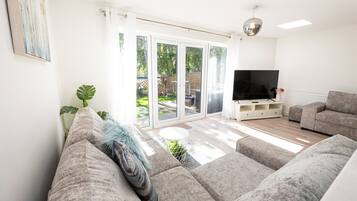 A living room with a grey sofa, a flat-screen TV, and a sliding glass door leading to a patio.