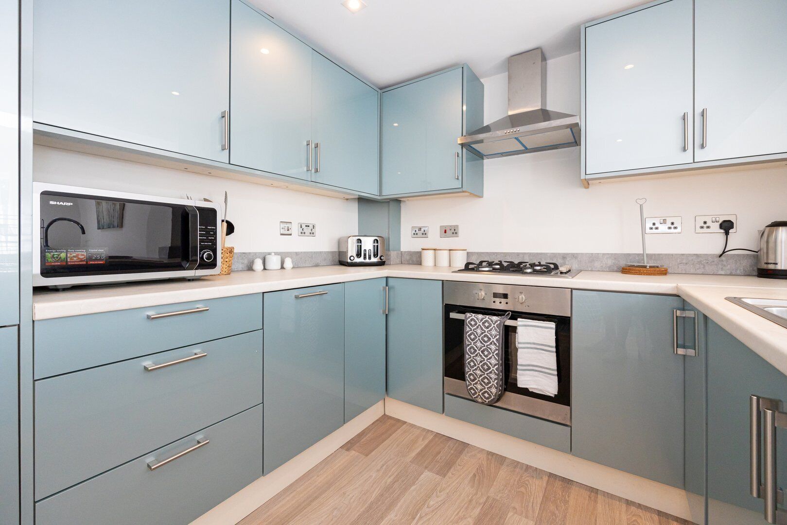 A modern kitchen with light blue cabinets, a microwave, a toaster, a stove, and a kettle.