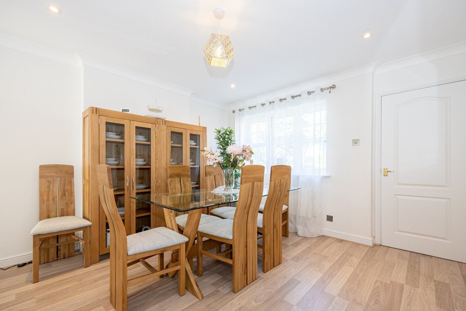 A dining area with a glass table, wooden chairs, and a cabinet with glass doors.