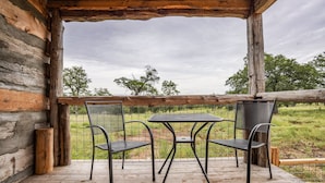 Eine Holzterrasse mit Tisch und zwei Stühlen, mit Blick auf ein Wiesenfeld.