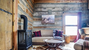 Ein Blockhaus-Interieur mit einer Couch, einem Tisch, einem Kamin und einem Fenster mit Vorhängen.