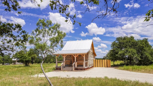 Eine rustikale Holzhütte mit Metalldach, umgeben von Bäumen und blauem Himmel.