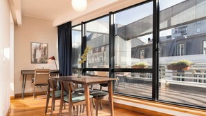 Ein stilvoller Essbereich mit einem Holztisch und Stühlen, einer Blumenvase und Blick auf Gebäude durch große Fenster.