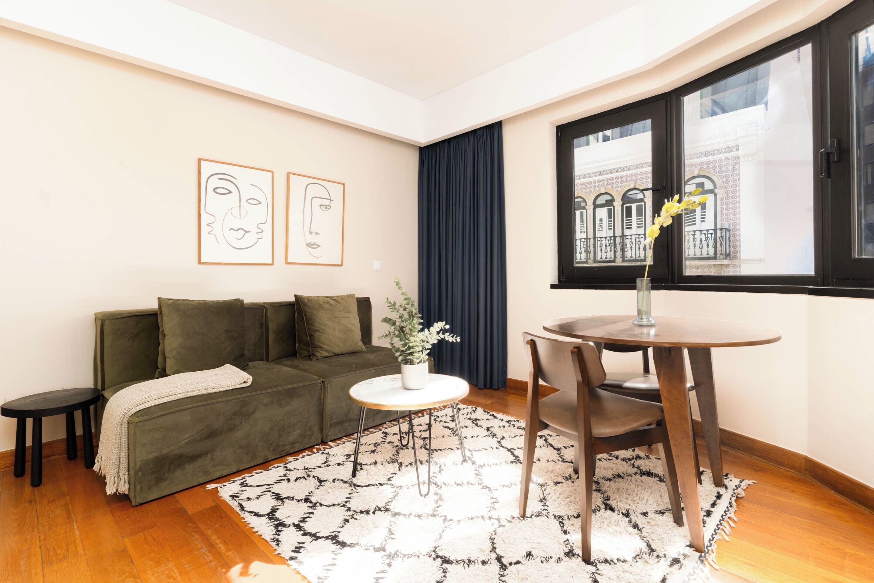 A living room with a sofa, a small round table with chairs, a potted plant, and artwork on the wall.