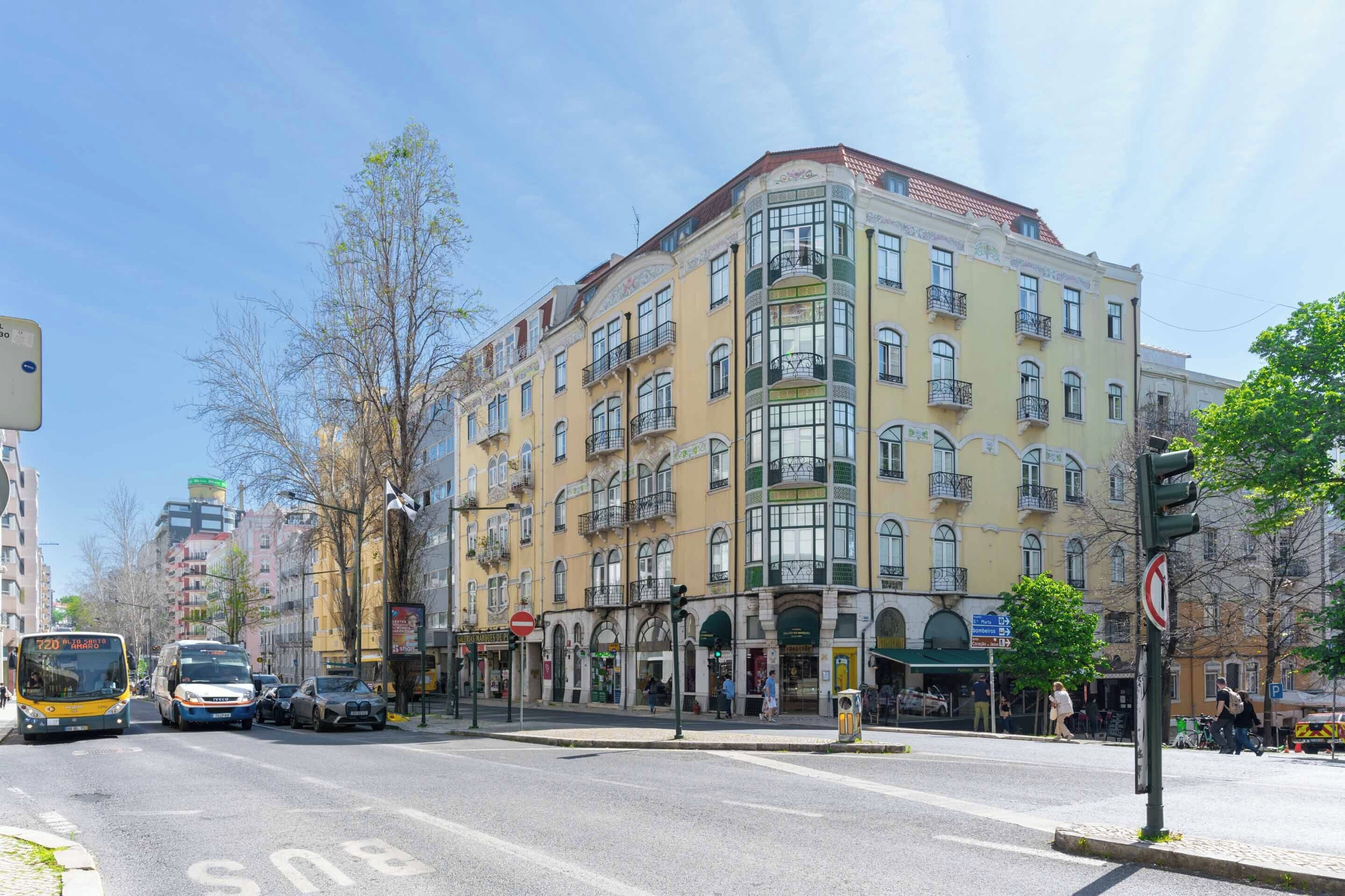 Un edificio de varios pisos con balcones, una parada de autobús y un paso de peatones.