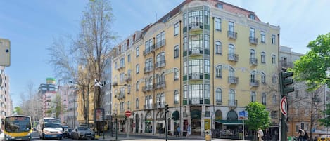 Un edificio de varios pisos con balcones, una parada de autobús y un paso de peatones.