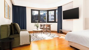 Ein modernes Hotelzimmer mit einer Couch, einem kleinen Tisch mit Stühlen, einem an der Wand befestigten Fernseher und einem großen Bett.