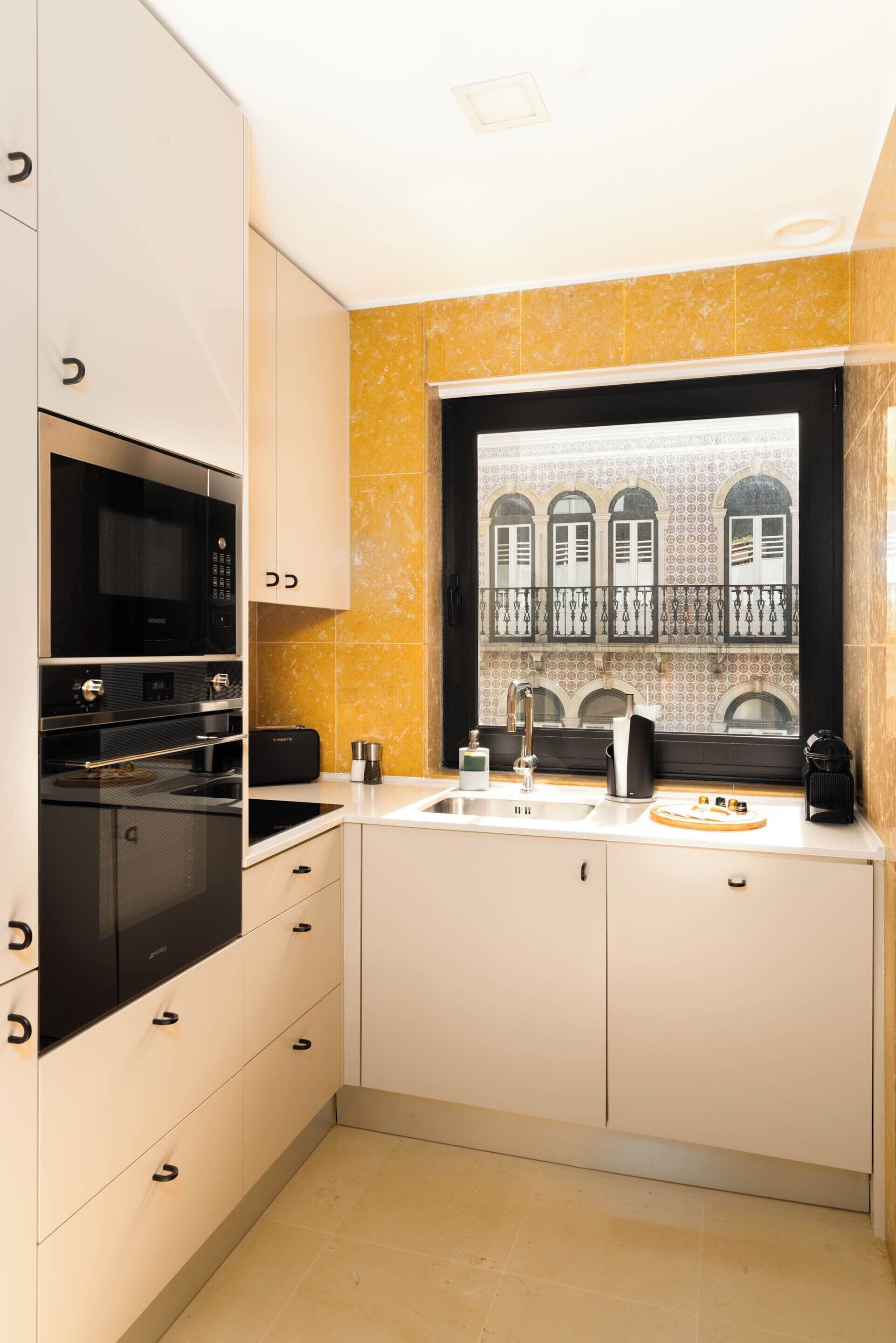 Una cocina moderna con armarios blancos, un microondas negro y una ventana con vistas a un edificio con ventanas arqueadas.