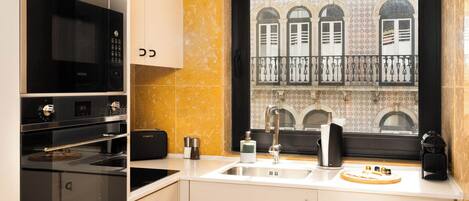 Una cocina moderna con armarios blancos, un microondas negro y una ventana con vistas a un edificio con ventanas arqueadas.