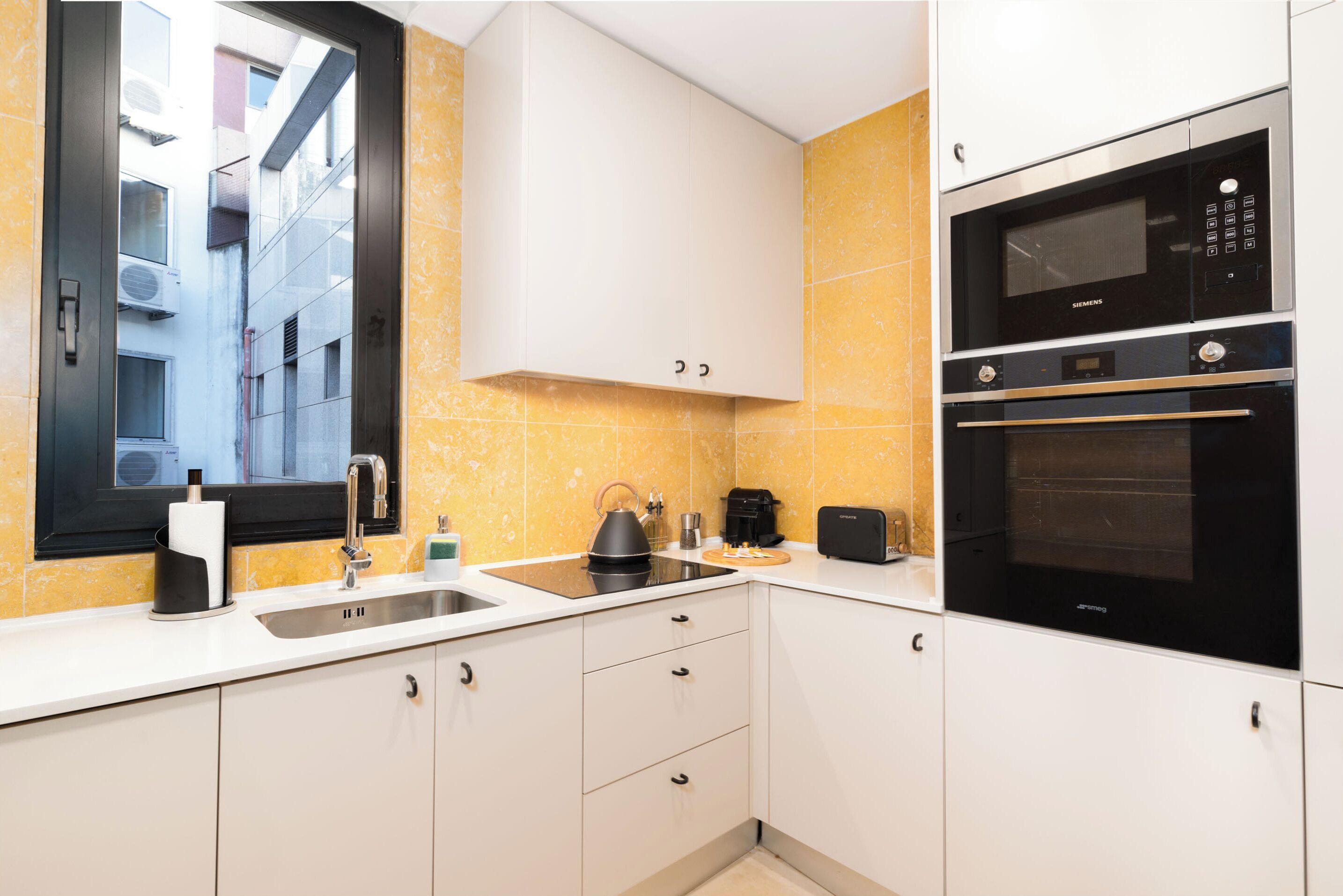 A modern kitchen with a sink, kettle, coffee maker, and a built-in oven.