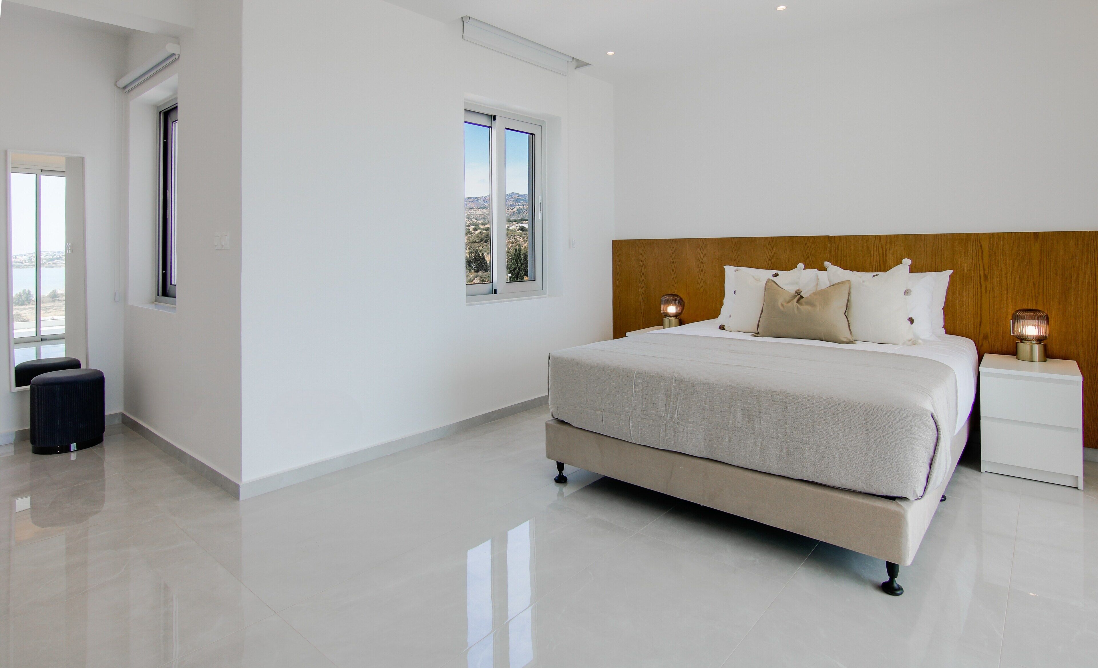 A modern bedroom with a large bed, a wooden headboard, and a nightstand with a lamp.