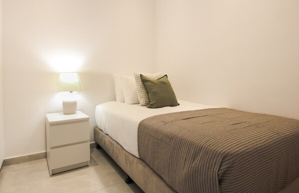 A neatly made bed with a brown striped blanket, a white pillow, and a green pillow on a white nightstand with a lamp. - Phaedrus Living: Luxury Seaview Coral Bay Villa (Pegeia)
