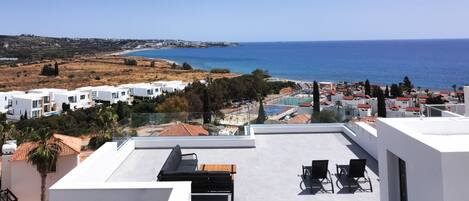 Eine Dachterrasse mit Blick auf das Meer, weiße Gebäude und einen Poolbereich.
