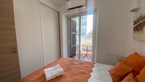 A bedroom with a bed, an air conditioning unit, a balcony with a table and chairs, and a painting on the wall. - Détendez Vous Dans cet Appartement 2 Pièces Calme Élégant Rénové Entièrement (Nice)