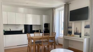 A modern kitchen with white cabinets, a dining table with chairs, a microwave, and an oven. - Détendez Vous Dans cet Appartement 2 Pièces Calme Élégant Rénové Entièrement (Nice)