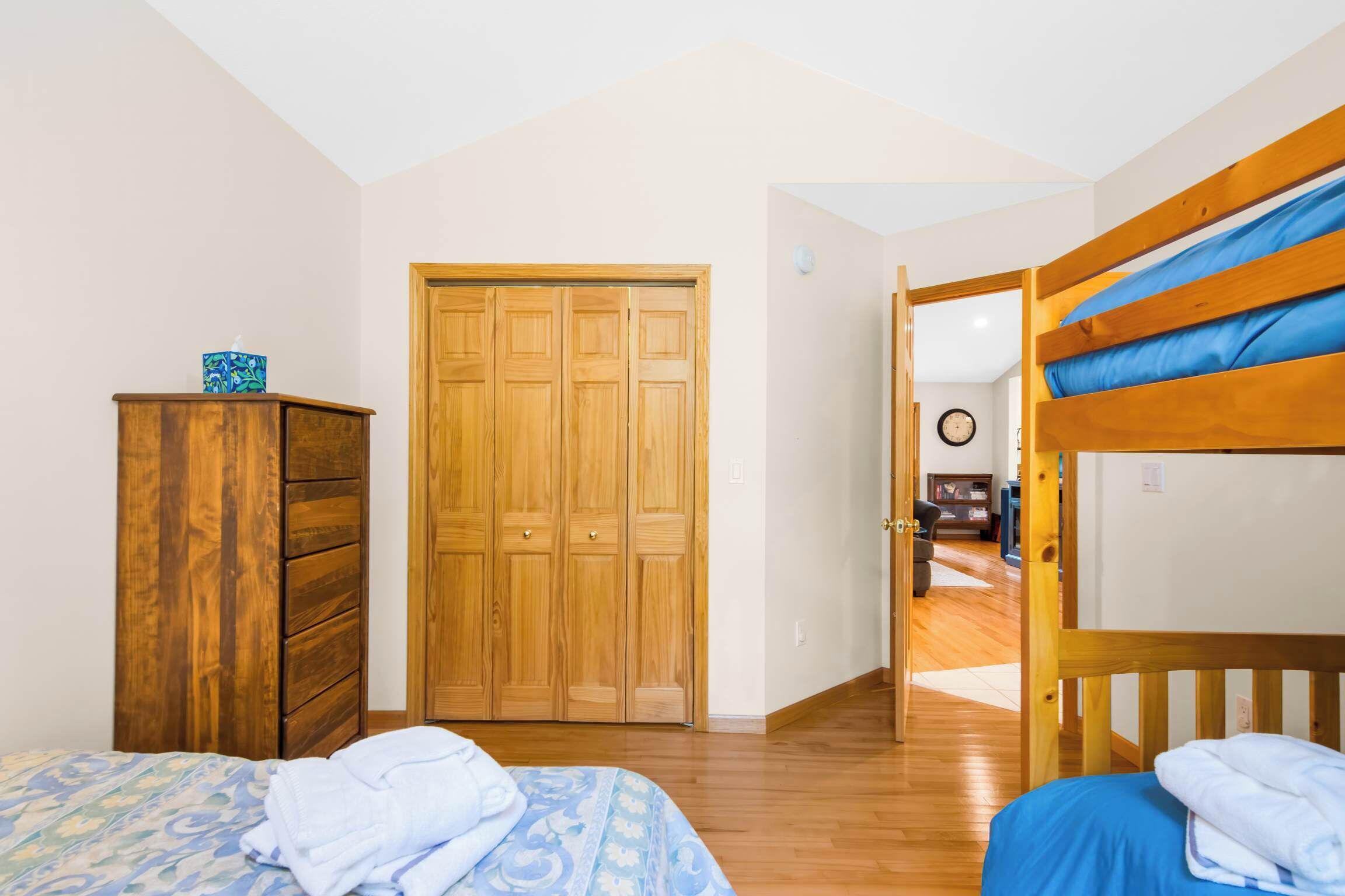 Une chambre avec deux lits, une armoire en bois et une porte donnant sur une autre pièce.