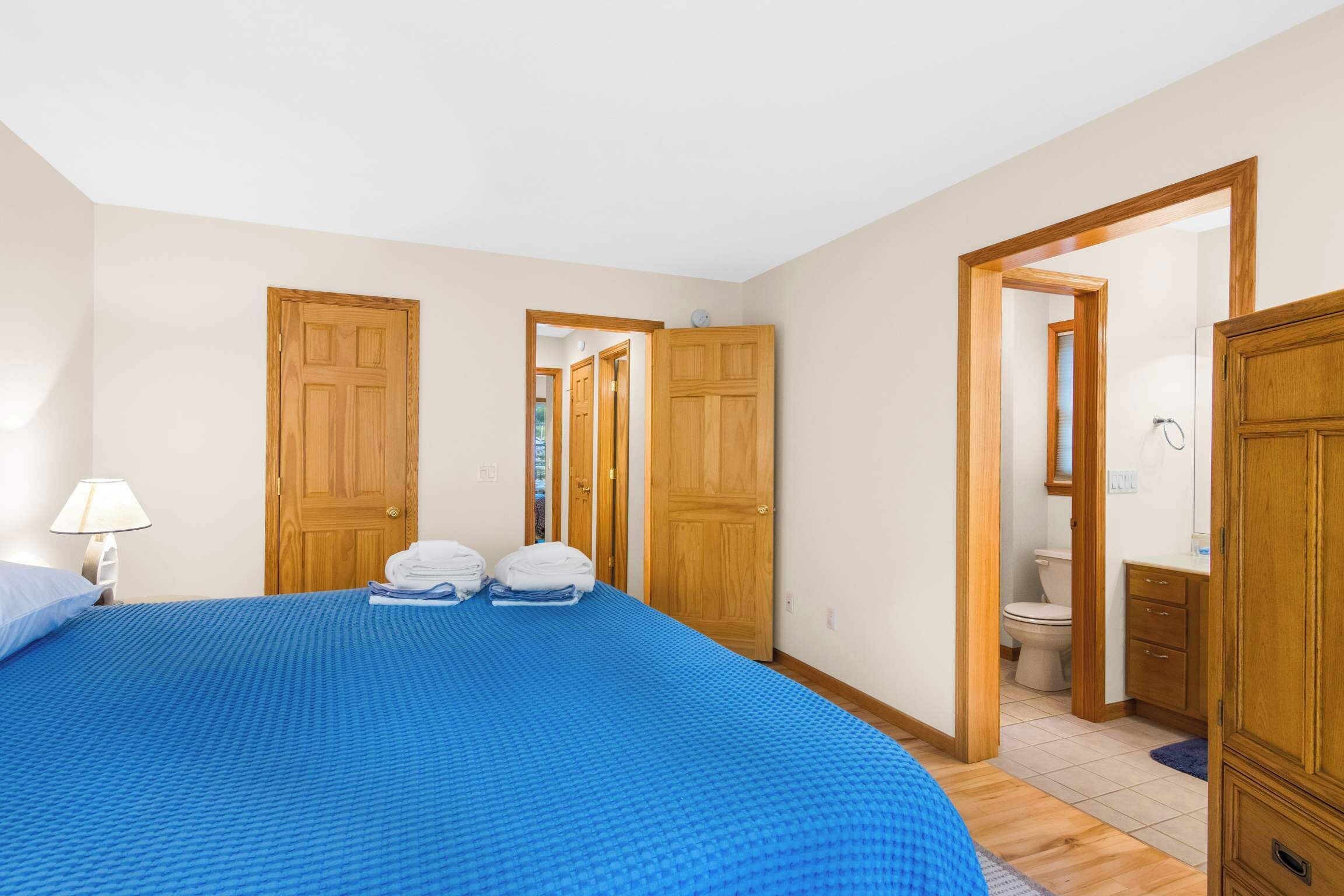 A hotel room with a large bed, wooden doors, a bathroom, and a small desk.