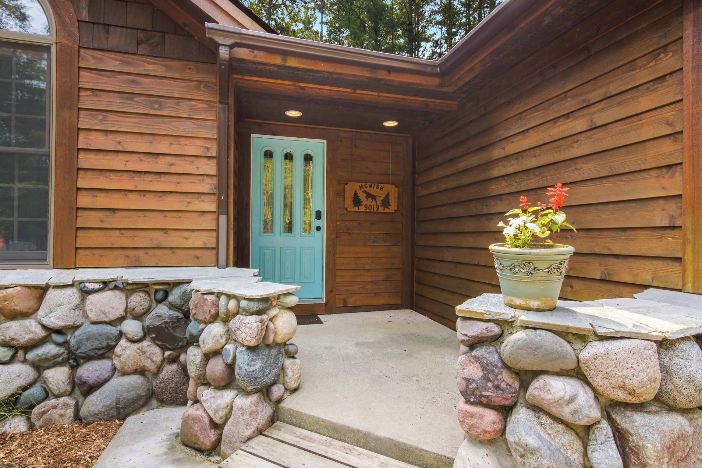 Una cabaña de madera con entrada de pared de piedra, una puerta azul y un letrero con un ciervo y árboles.