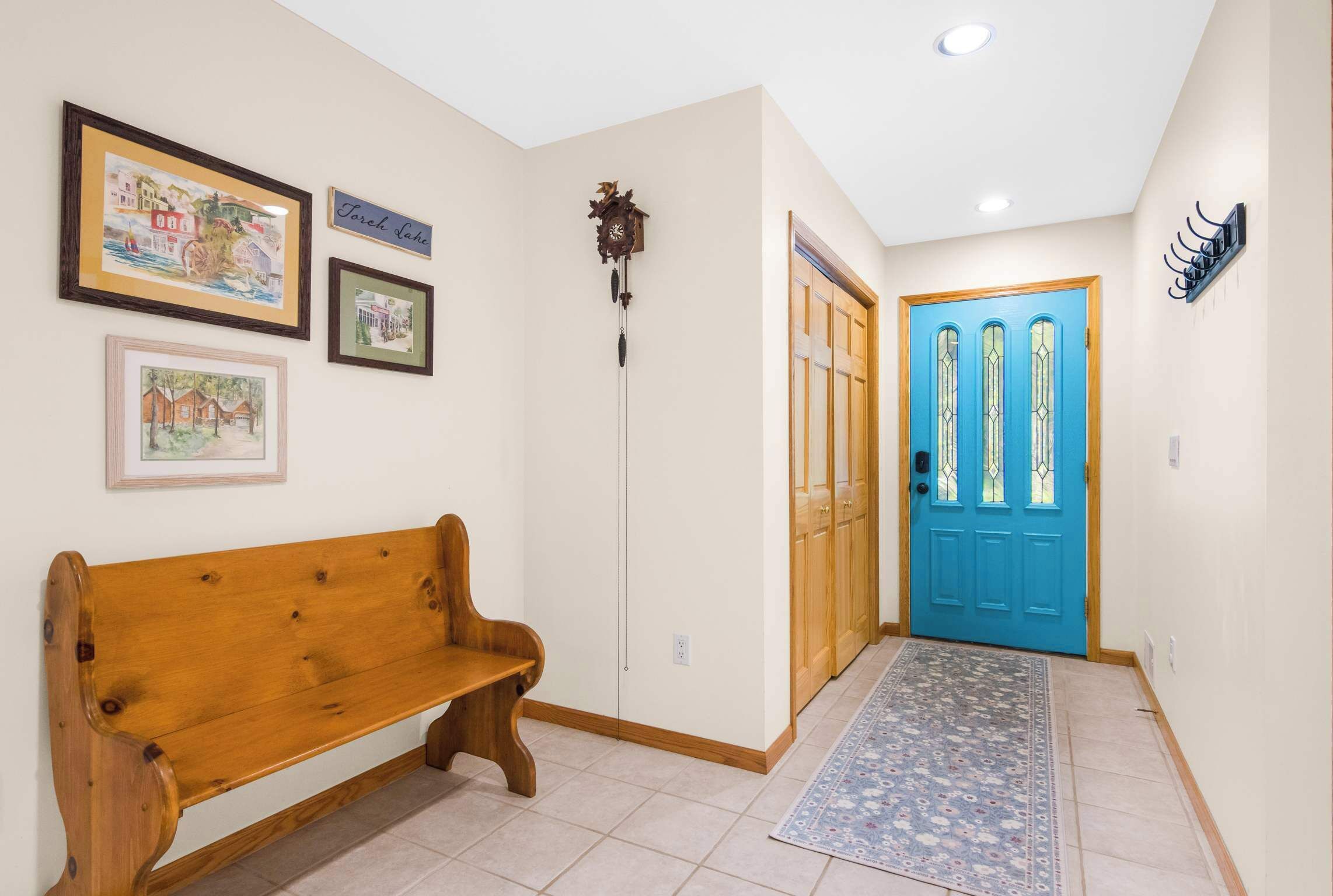 A hallway with a wooden bench, a blue door, and framed pictures on the wall.