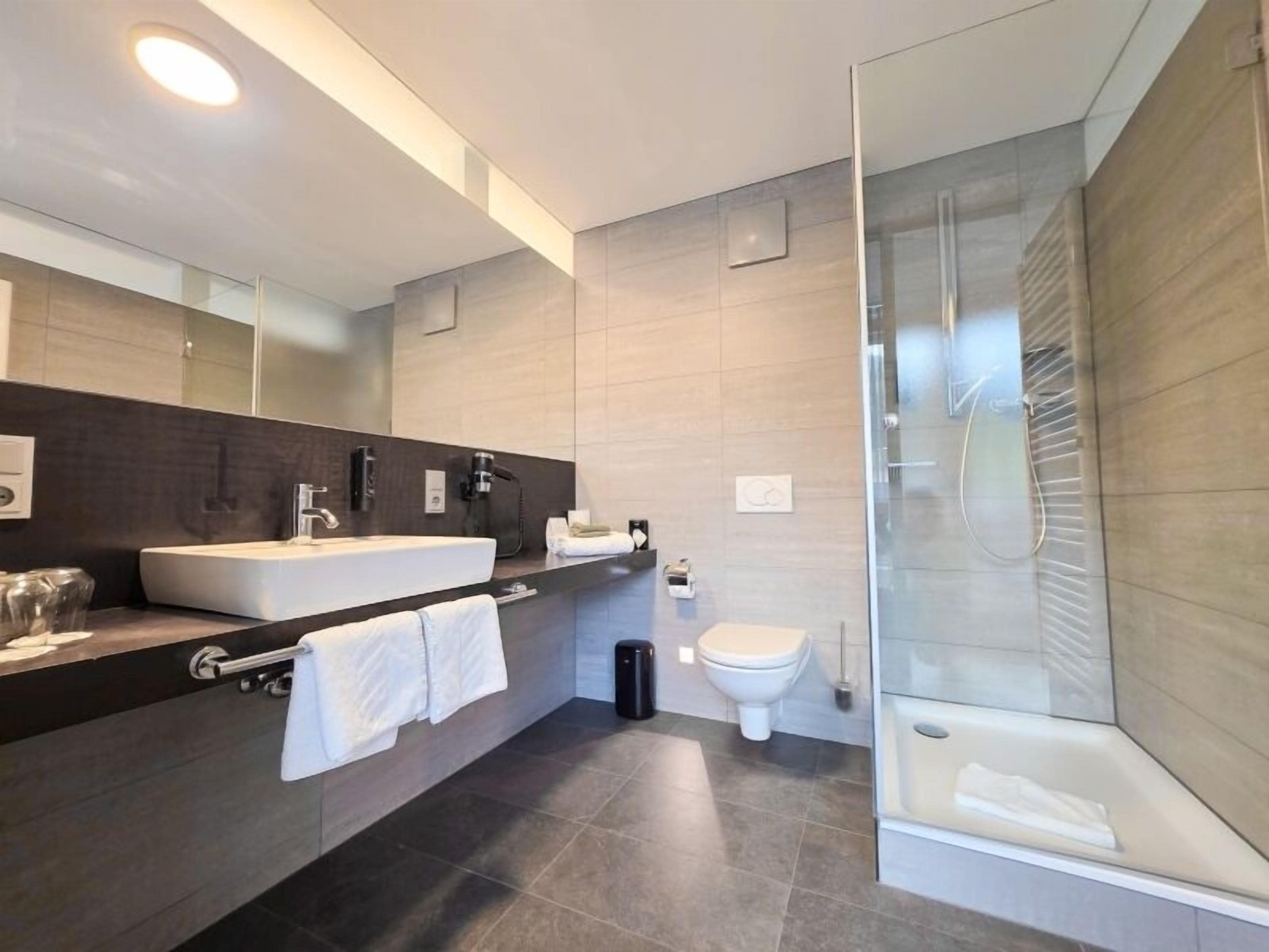 Une salle de bain moderne avec un grand miroir, deux lavabos, des toilettes et une douche à parois de verre.