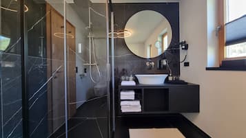 Ein modernes Badezimmer mit einer gläsernen Duschkabine, einem runden Spiegel, einem weißen Waschbecken und einem dunklen Waschtisch.