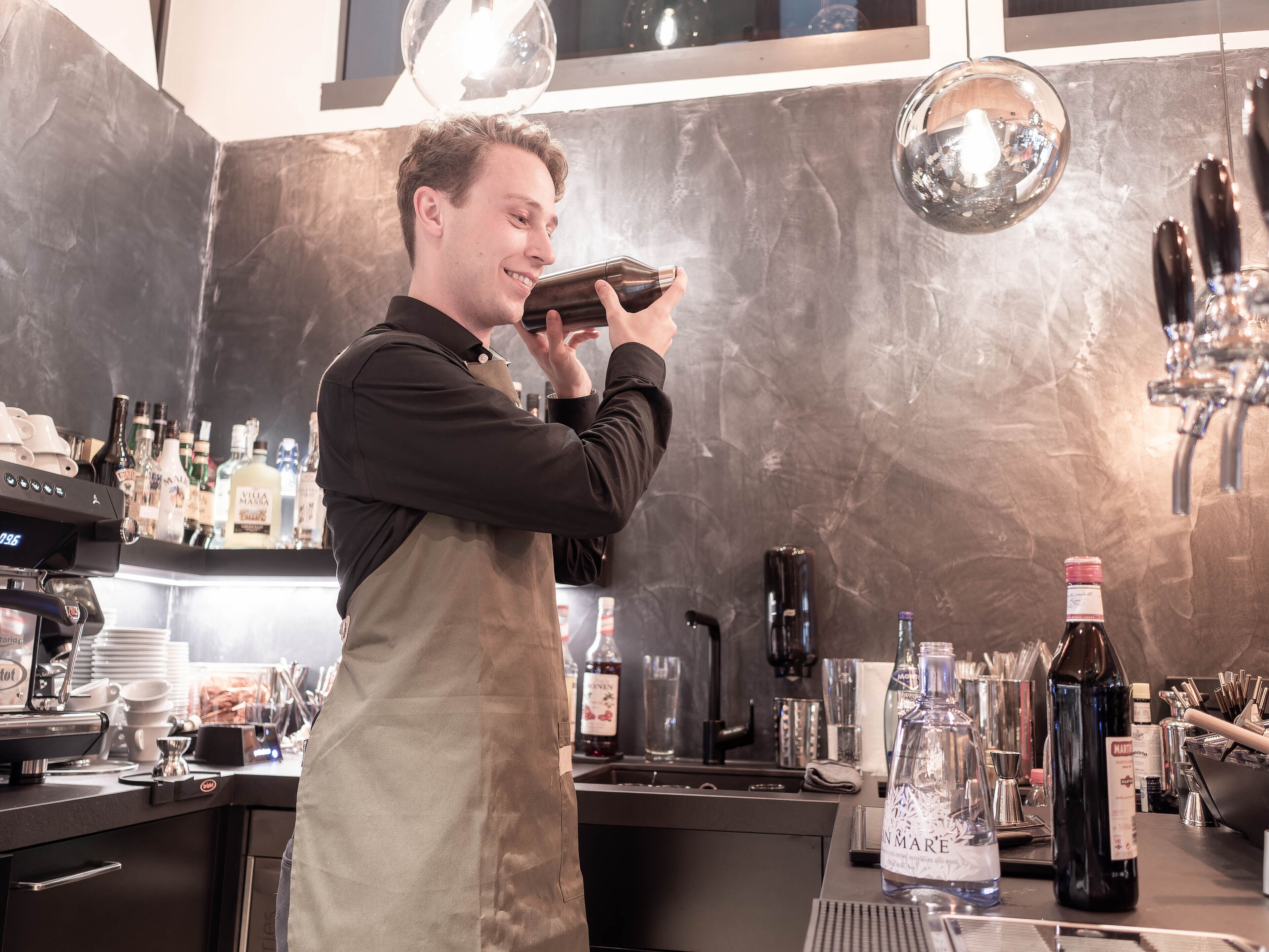 Eine Barista bereitet ein Getränk mit einer Kaffeemaschine und verschiedenen Barwerkzeugen zu.