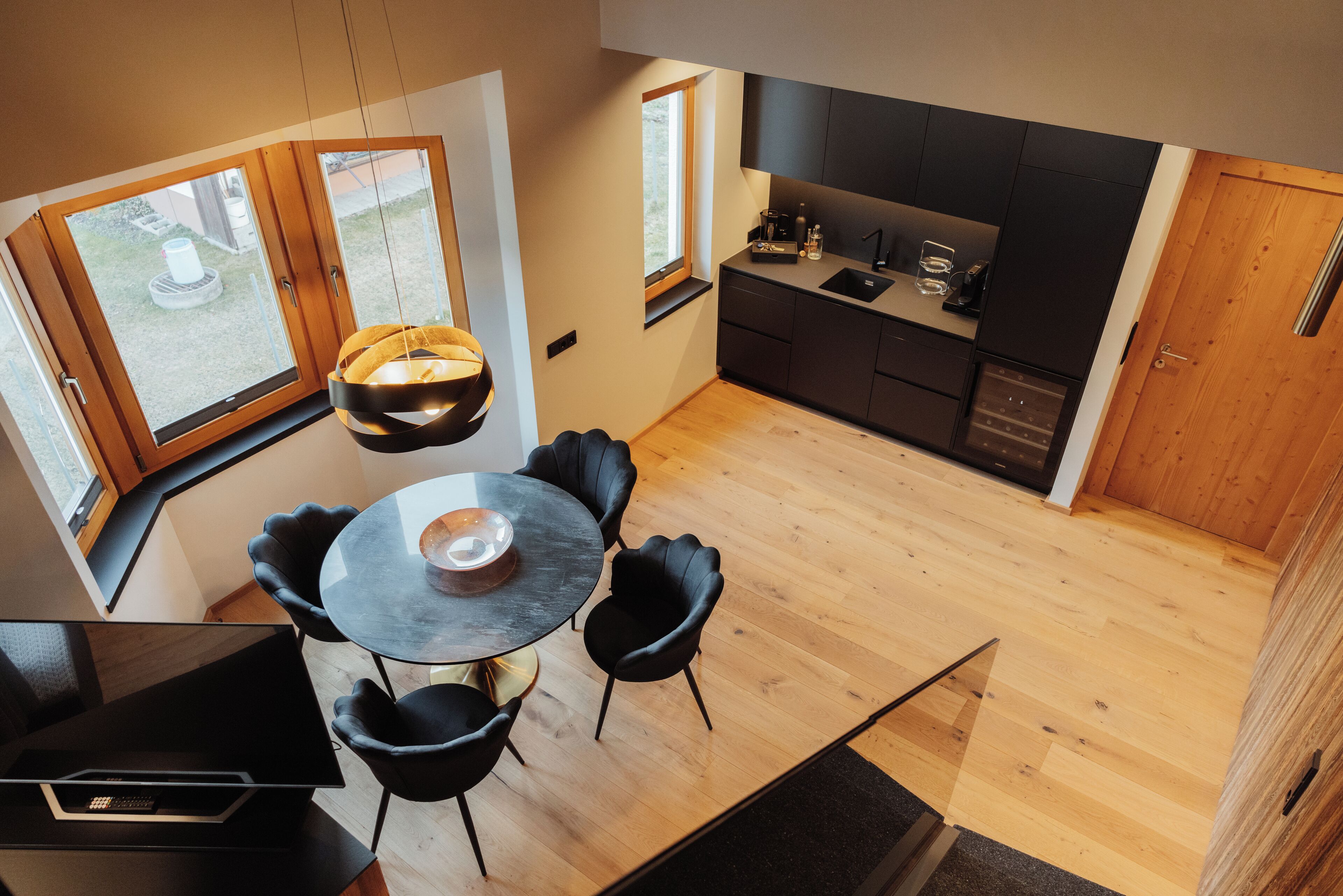 Una cucina moderna con mobili scuri, un'area pranzo con tavolo rotondo e sedie nere, e vista sull'esterno attraverso ampie finestre.