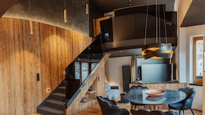 Een modern interieur met een houten trap, een eetruimte met een ronde tafel en stoelen, en een keuken met een groot kookeiland.