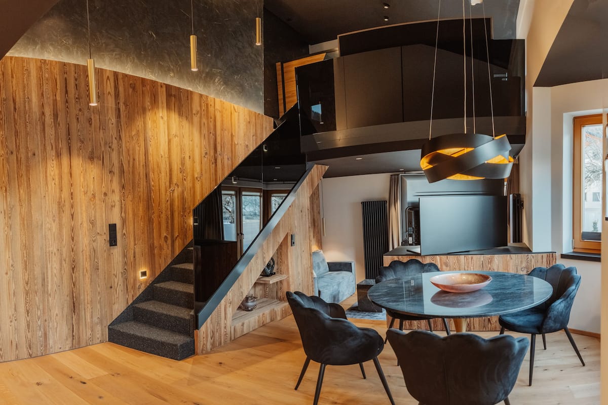 Un interior moderno con una escalera de madera, un comedor con una mesa redonda y sillas, y una cocina con una isla grande.