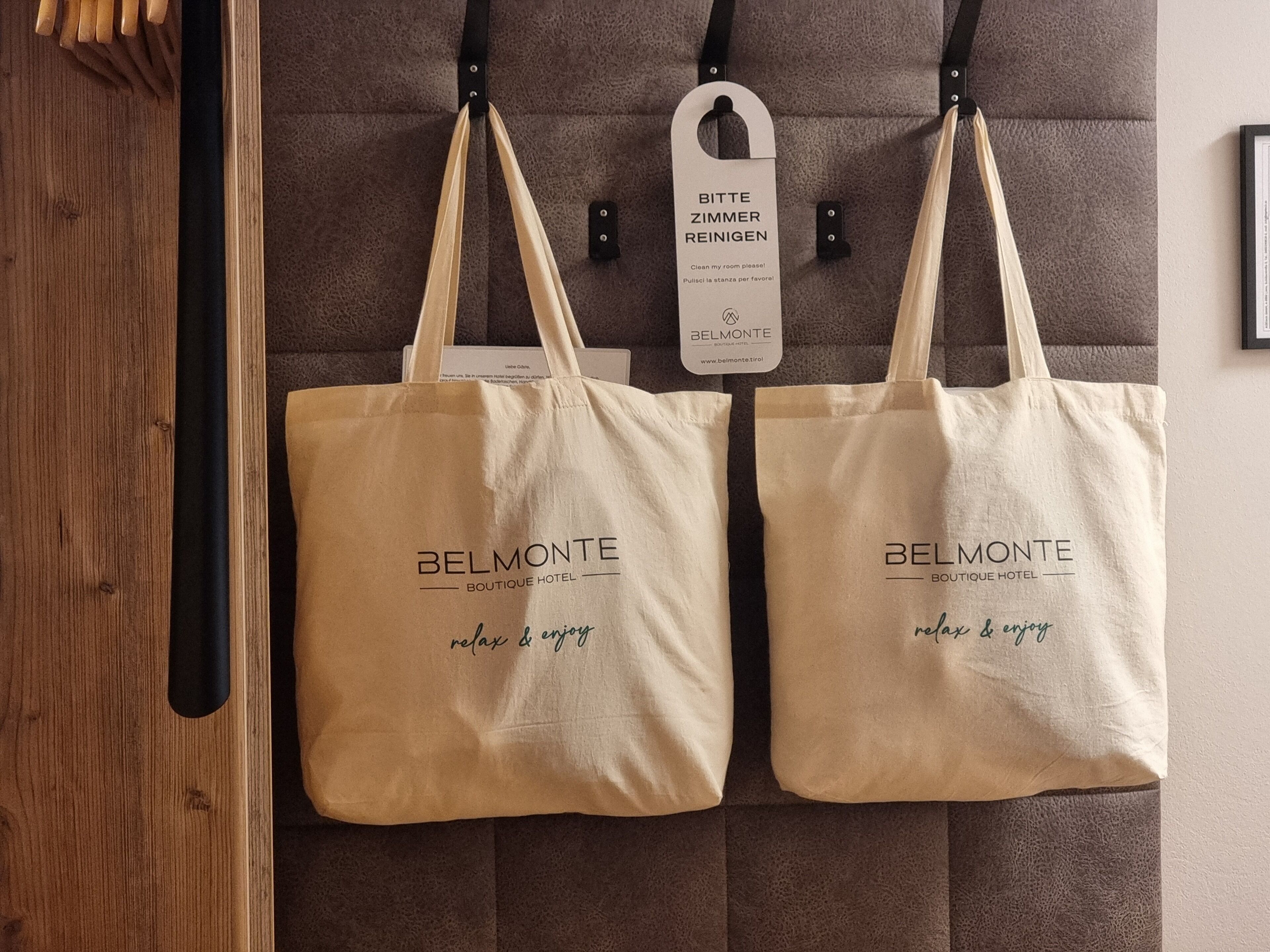 Dos bolsas de tela color beige del hotel boutique BELMONTE colgadas en una pared, con un cartel que indica limpiar la habitación.