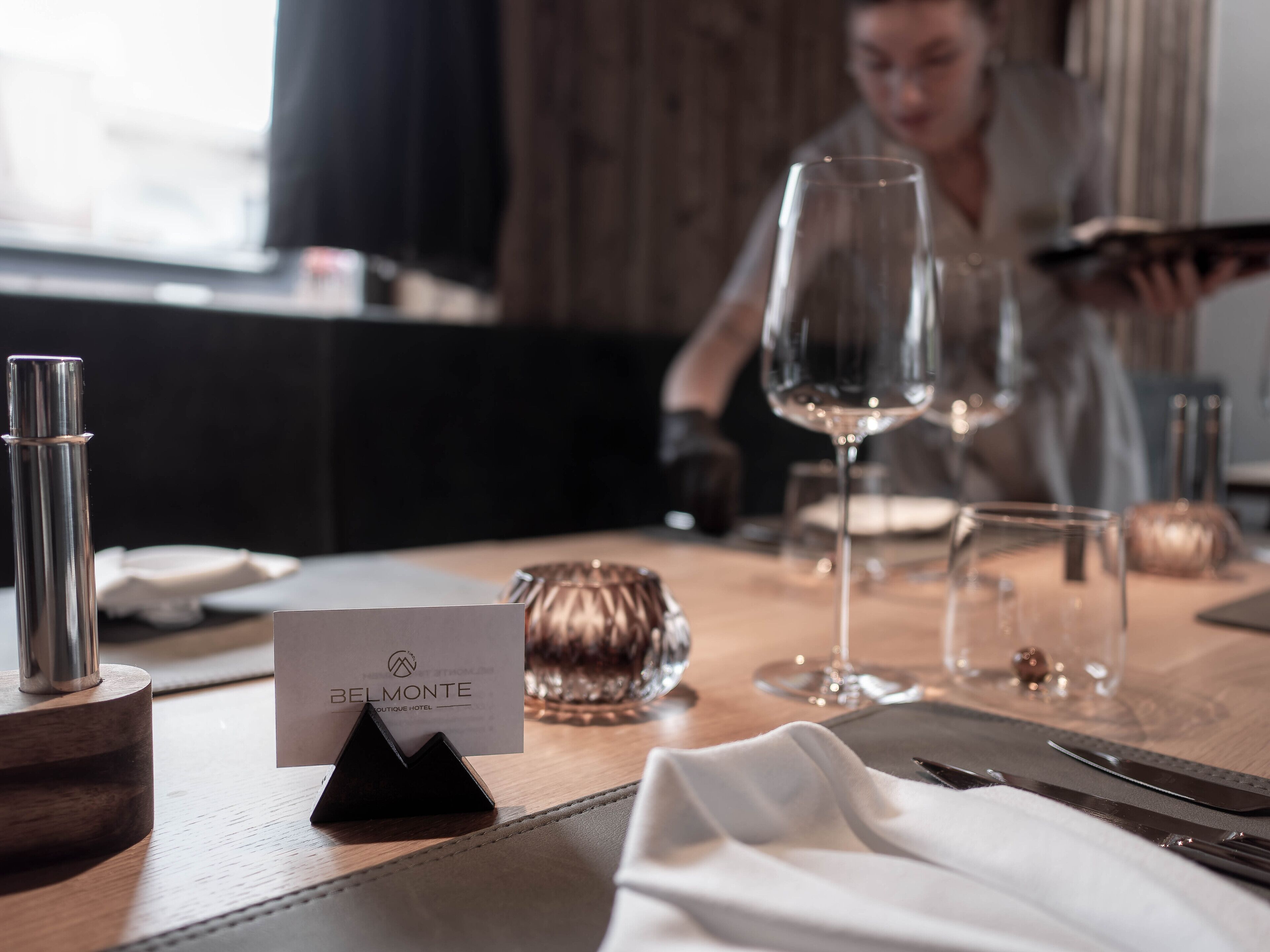 A neatly set dining table with a 'BELMONTE' sign, a wine glass, and a candle.