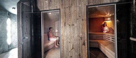 A sauna room with wooden walls and benches, a glass door, and a tiled floor.