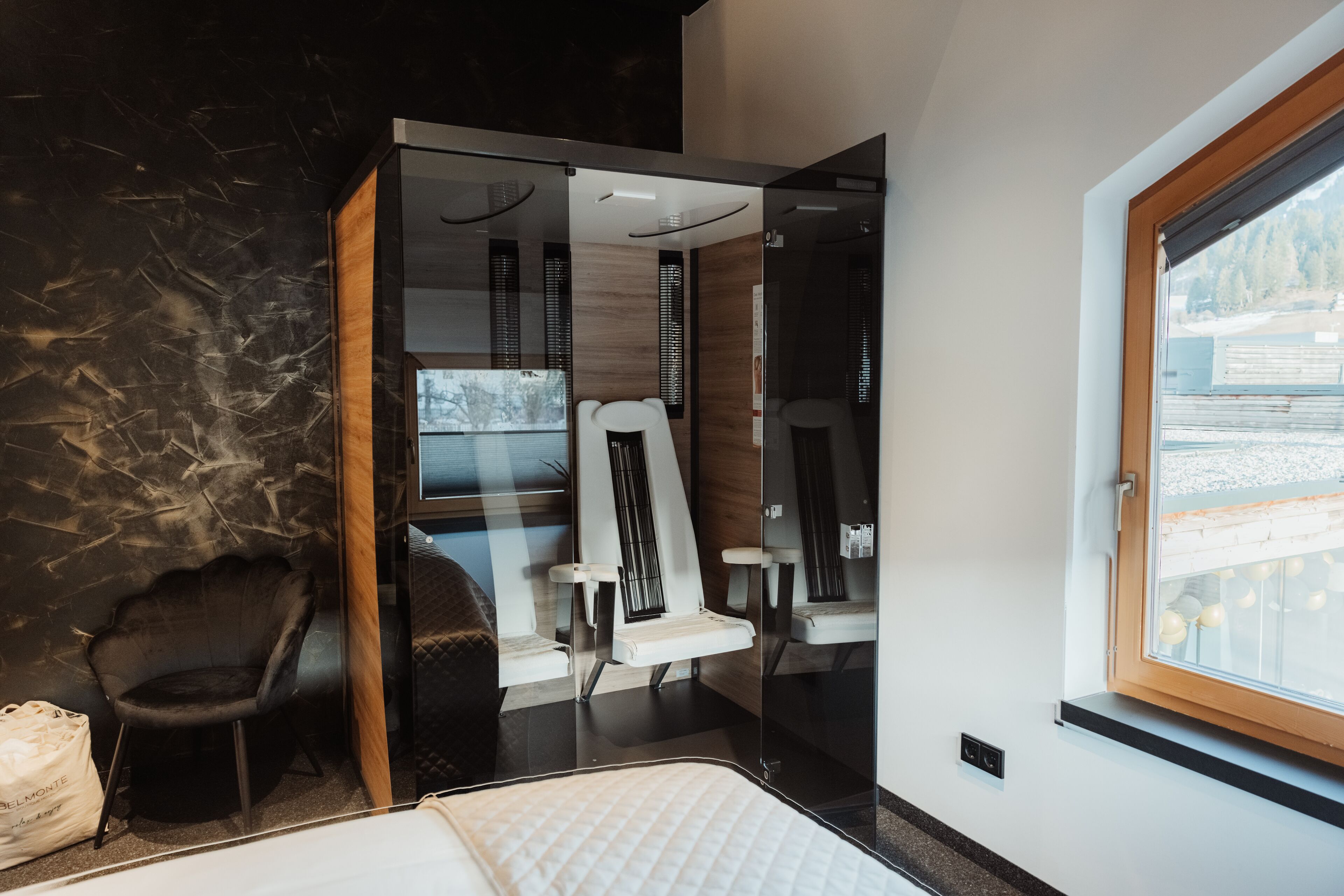 A modern room with a bed, a glass partition, a chair, and a window.