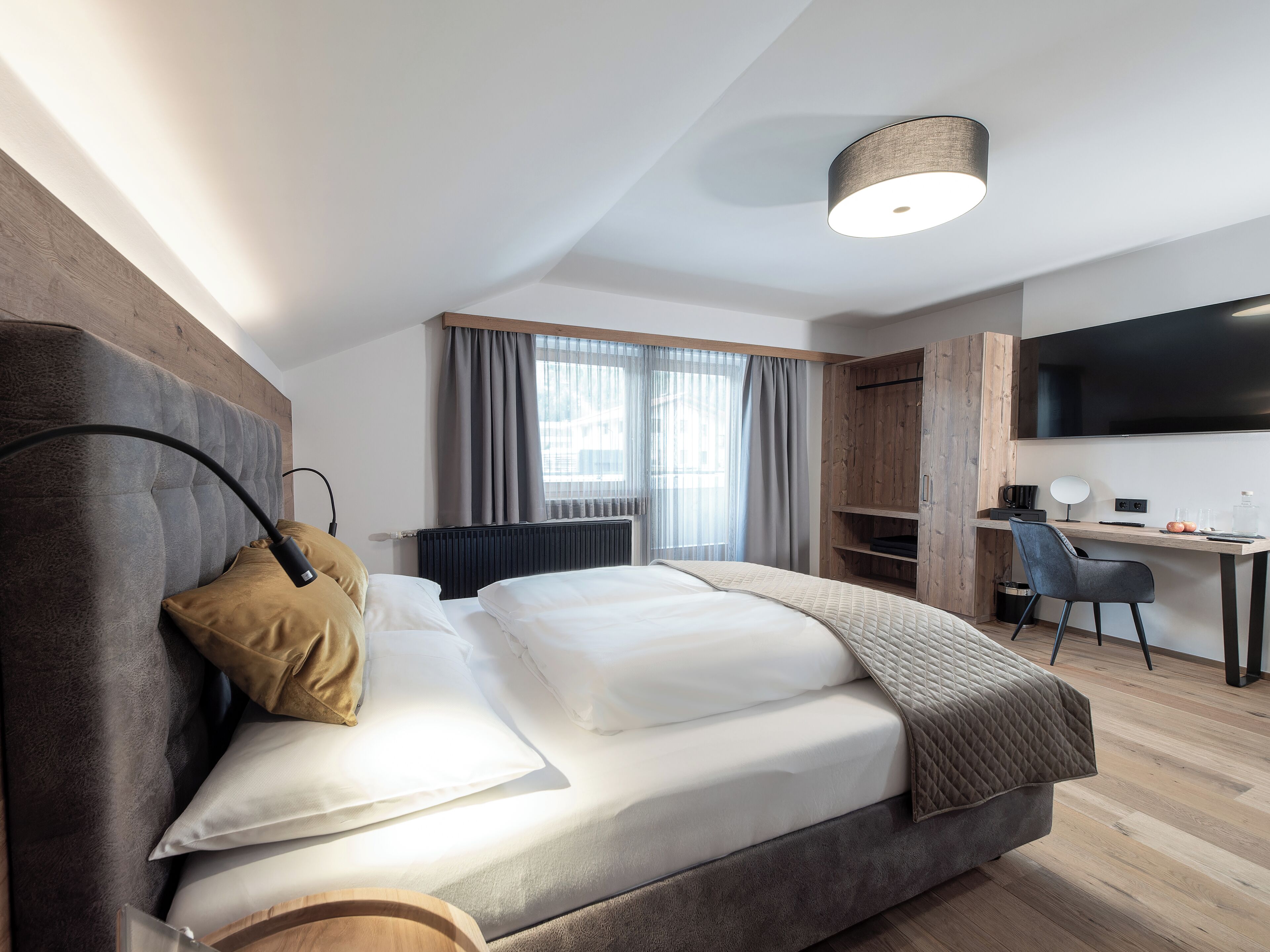 Ein modernes Hotelzimmer mit Bett, Schreibtisch, Stuhl und Fernseher.