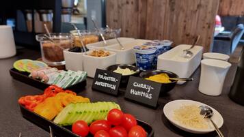 En buffet med mærkede retter, herunder 'Kräuter-Austrian', 'Curry-Hummus' samt et udvalg af frugter og grøntsager.