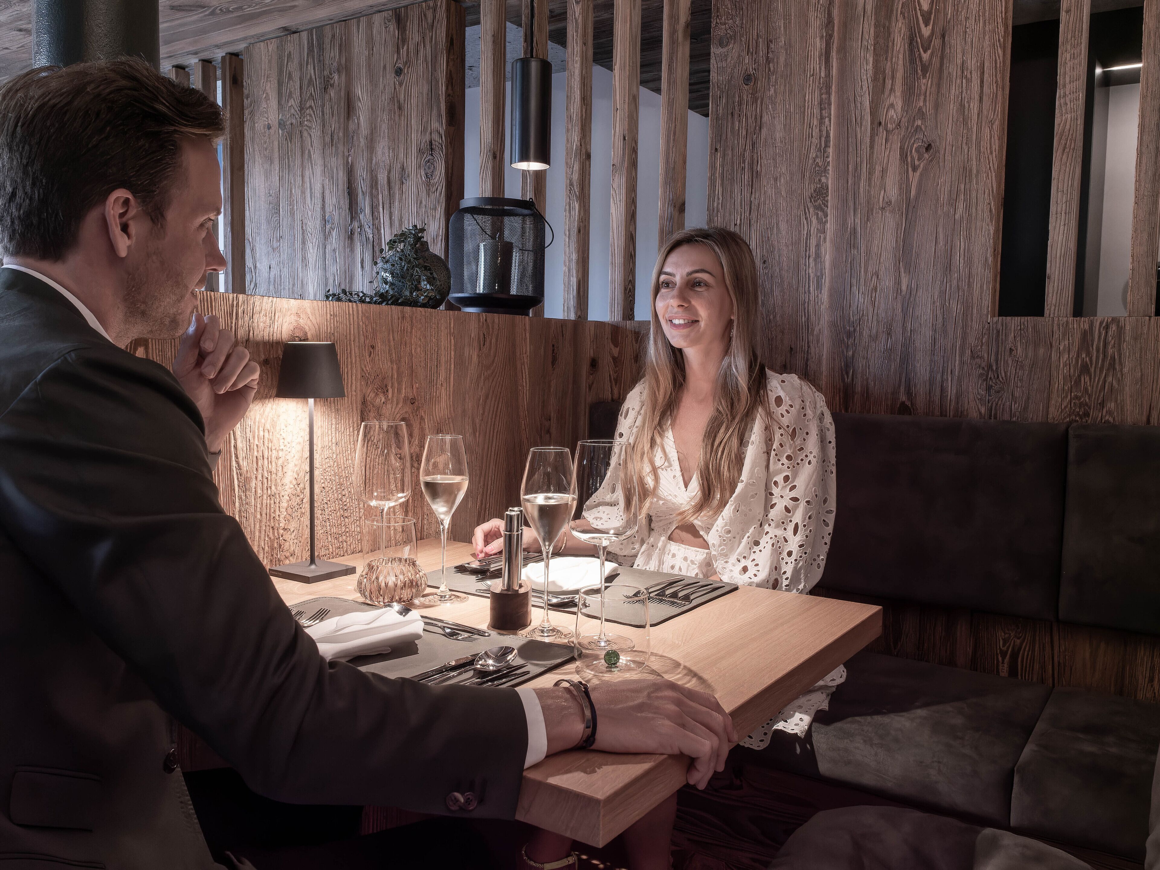 Un intérieur en bois avec une table à manger dressée pour deux personnes, agrémentée de verres à vin et de couverts.