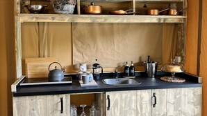 A rustic kitchen with wooden cabinets, a black countertop, and copper cookware. - Kingfisher Safari Tent (Droitwich)