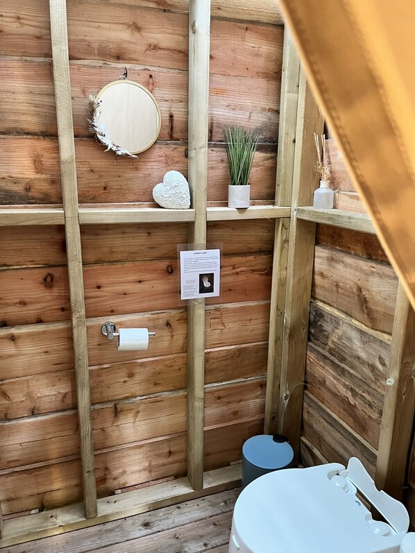 A wooden cabin bathroom with a toilet, a small sink, and a mirror.