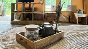 A cozy room with a large window, a wooden TV stand, a woven rug, and a wooden side table with a vase. - Kingfisher Safari Tent (Droitwich)