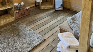 A cozy room with wooden floors, a large window, a wooden bench, a small table with a basket, and a hanging robe.