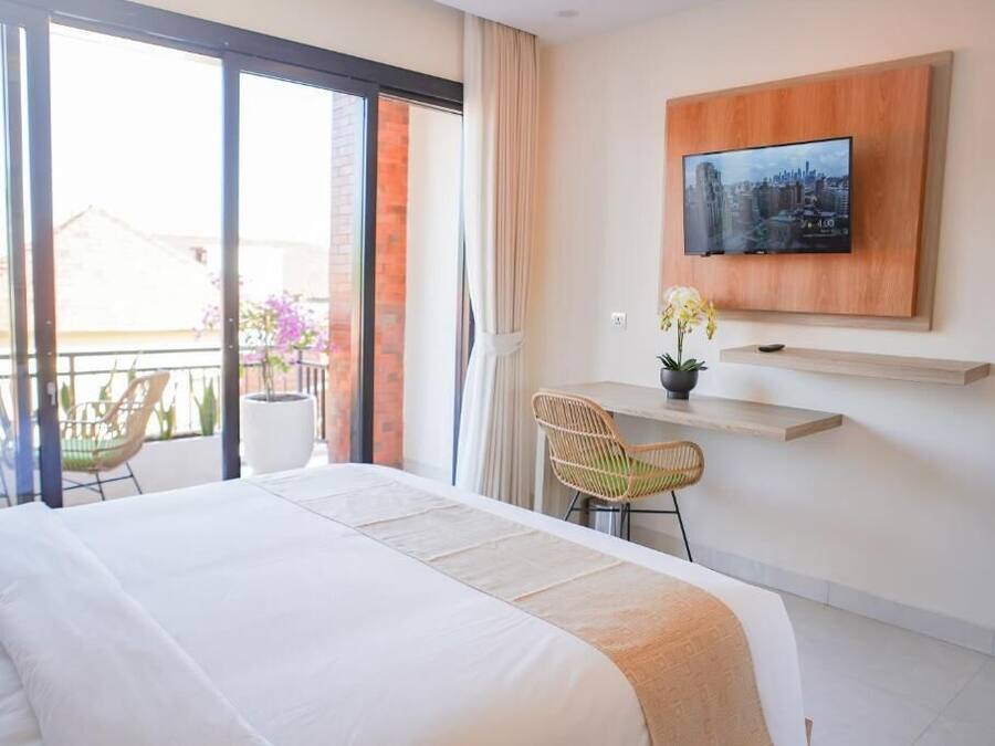 Habitación de hotel con cama, escritorio, silla, televisor montado en la pared y balcón con sillas y plantas.