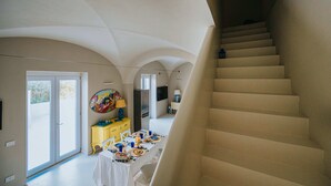 Un interior espaiós amb una escala, una zona de menjador amb taula posta per a un àpat, i una cuina amb nevera i televisió.