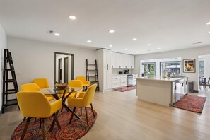 A modern kitchen with white cabinets, a central island, and a dining area with yellow chairs and a glass table. - Lakefront Haven w/ Pool! (Melrose)