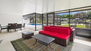 Et moderne udeområde med en rød sofa, fletmøbler, en pool med glasvægge og udsigt over det omkringliggende landskab.