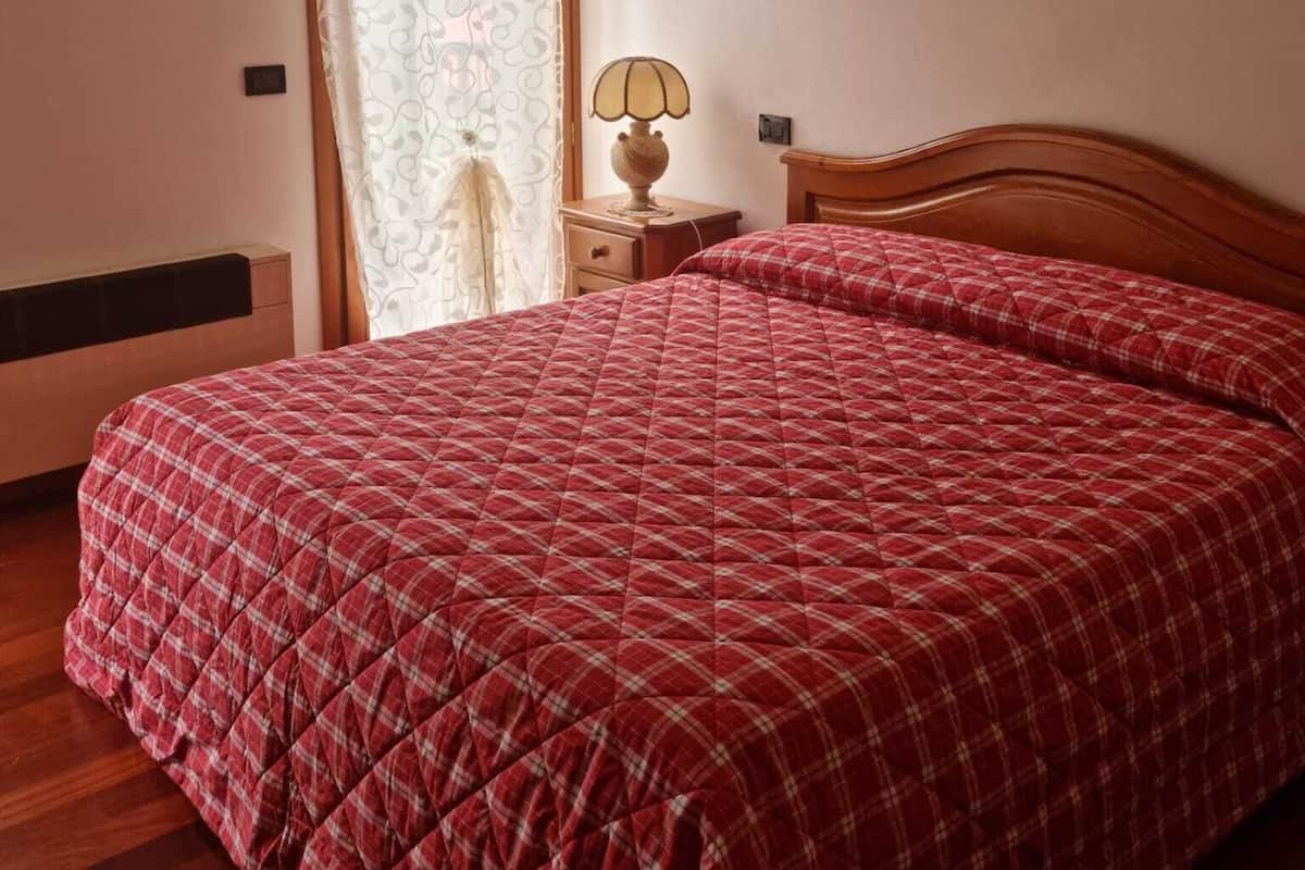 Ein Schlafzimmer mit einem hölzernen Bett, einem Nachttisch mit Lampe und einem Fenster mit Vorhängen.