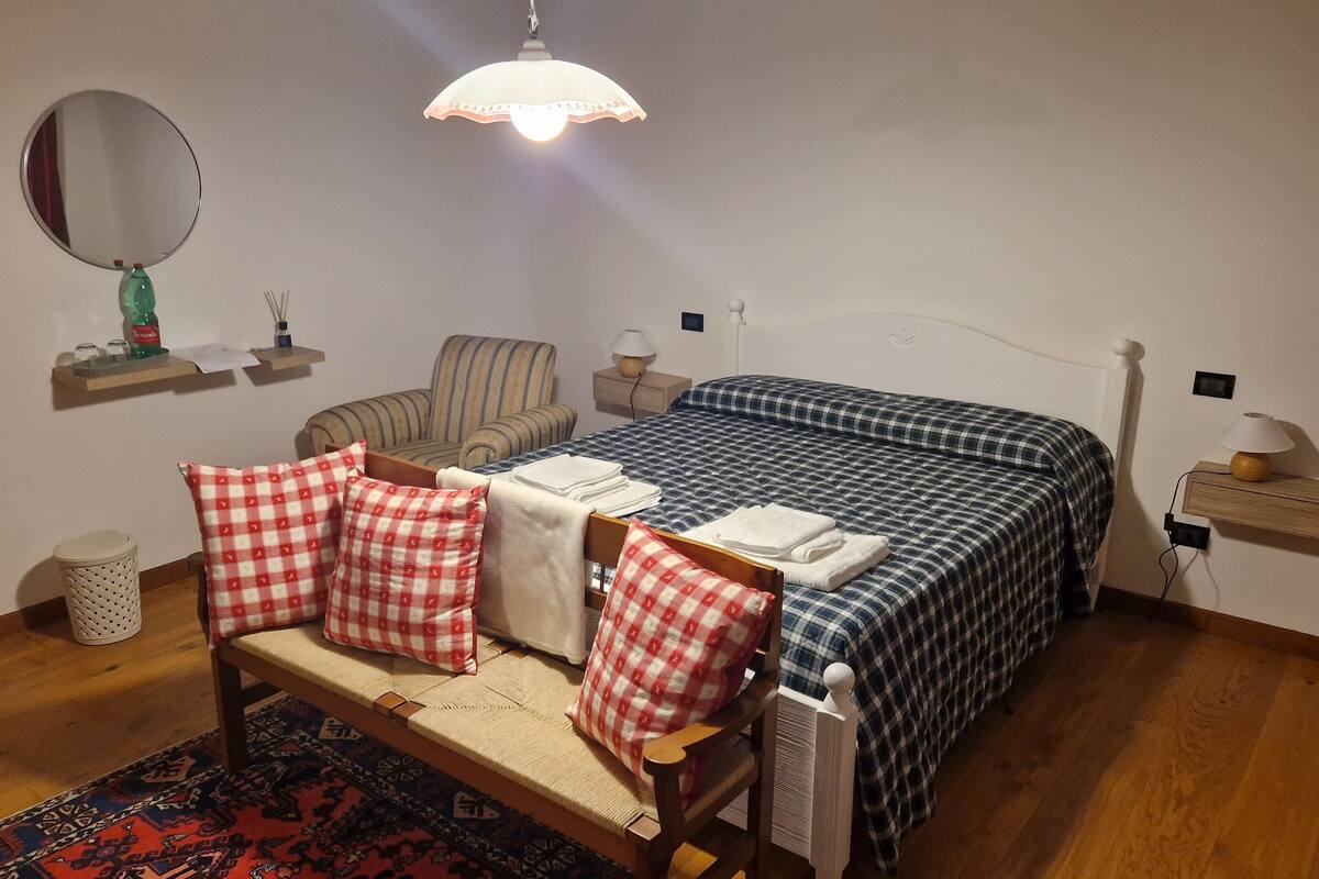 Ein Schlafzimmer mit einem Bett, einem Sessel, einem kleinen Tisch, einer Lampe und einem Spiegel.