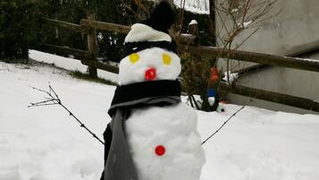 Un muñeco de nieve con bufanda negra y sombrero, de pie en un espacio exterior nevado.