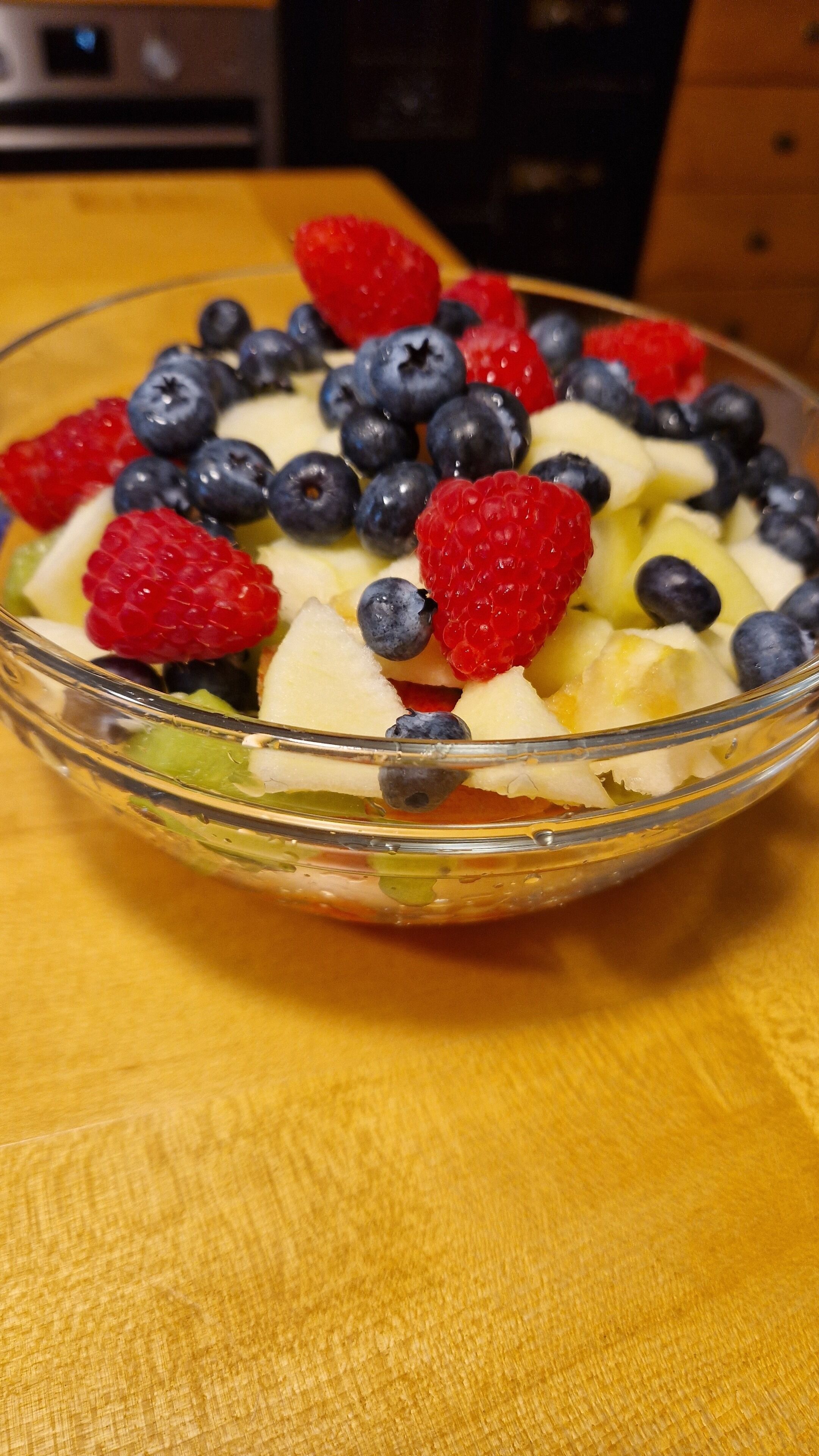 A clear glass bowl filled with a fruit salad on a wooden surface.