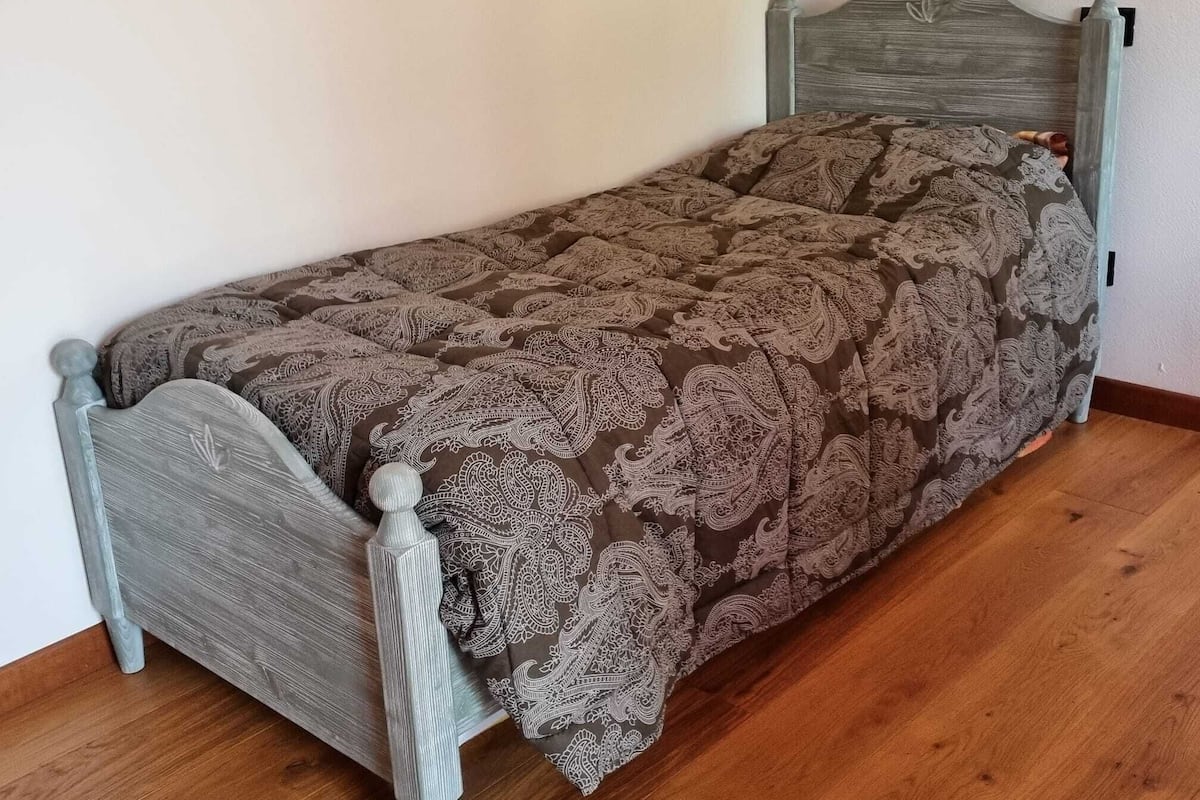 Ein Einzelbett mit einem gemusterten Bettüberwurf, einem Holz-Kopfteil und einem Holzboden.